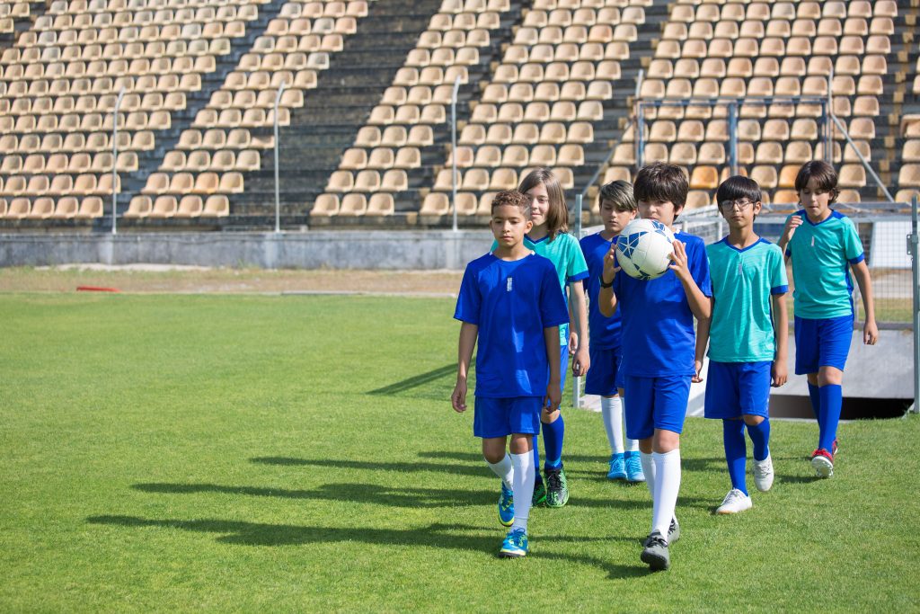 Group of boys in soccer uniforms walking on a grassy field during the day.